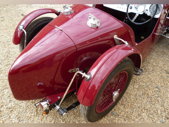 Rear three-quarter view of the finished car on gravel, showing the tapered tail and red wire wheels.