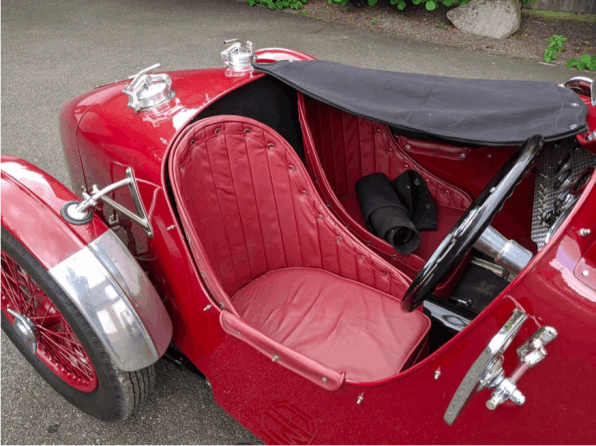 The cockpit seen from above, with red pleated leather seats, the hood folded down and the steering wheel.
